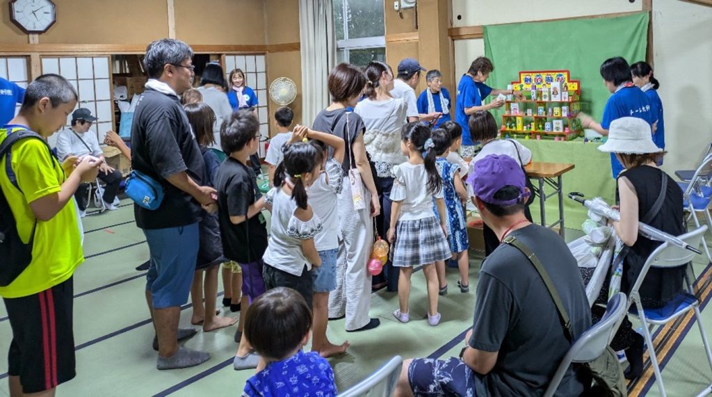 射的ブースにて景品を並べているスタッフと順番待ちをしているたくさんの親子