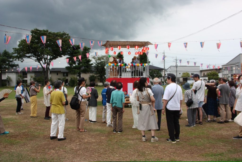 櫓の上で演奏する祭半被を着た３人の人たちとその演奏を見ている人たち